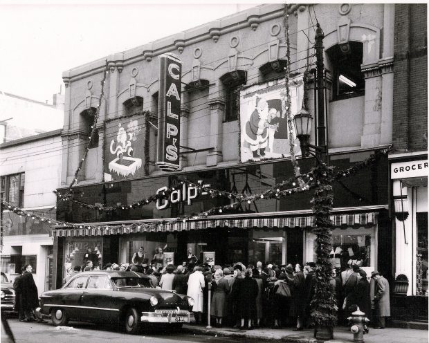 Vue extérieure du magasin Calp’s avec de grands panneaux au dessus de la porte, des décorations de Noël et une grande file de clients attendant d’entrer.