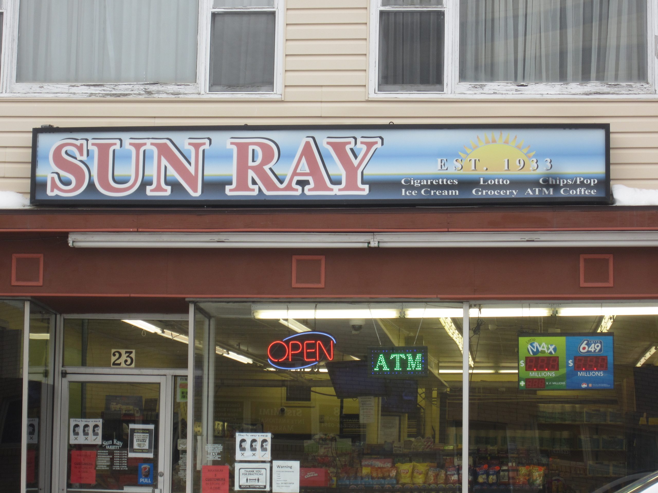 Entrée du dépanneur Sun Ray avec deux grandes fenêtres en verre et une porte. 