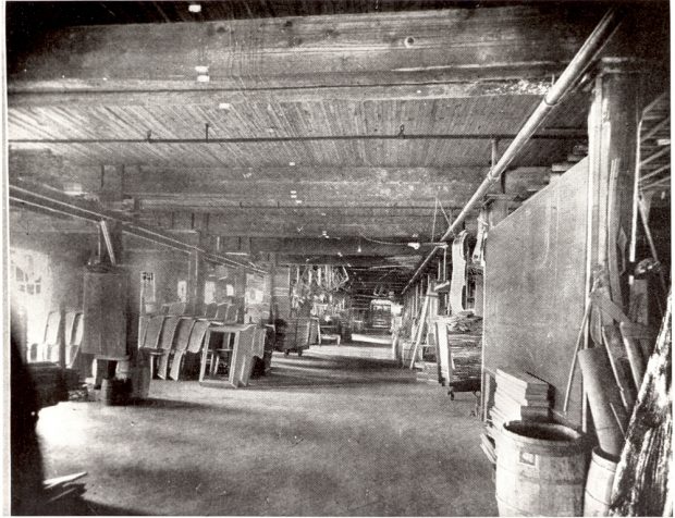 Une pièce d'une usine. Des outils et des caisses de calèches en bois sont empilés le long des murs.