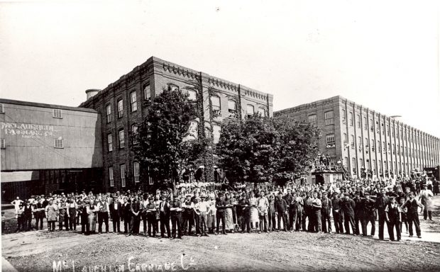 Une foule constituée de plusieurs centaines d’employés pose devant une série de grands bâtiments industriels.