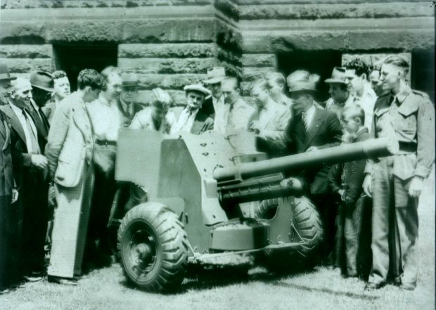 Image en noir et blanc d’une foule d’hommes, de femmes et d’enfants inspectant une pièce d’artillerie.