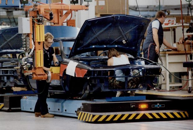 Image en couleur représentant trois hommes utilisant des machines-outils pour assembler une voiture sur une chaîne de montage.