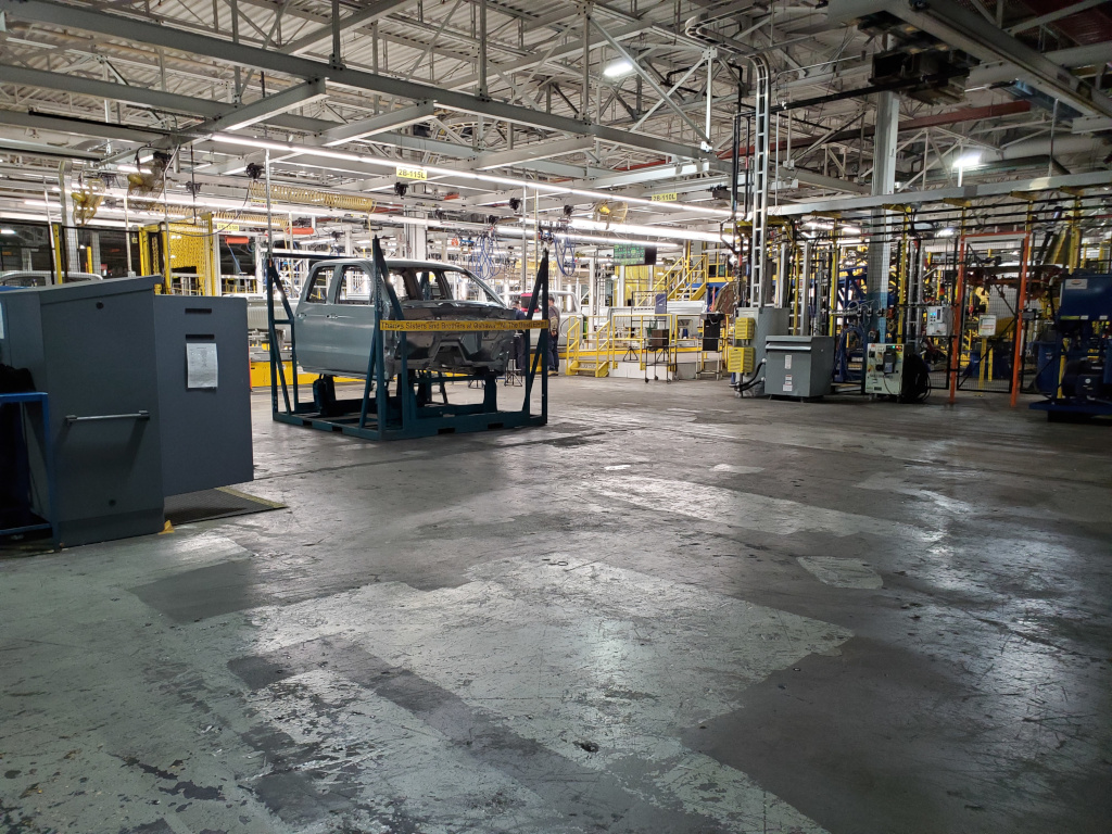 Photo en couleur d’une cabine de pick-up partiellement assemblée posée sur une palette dans un local industriel vide.