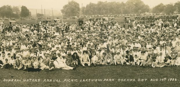 Image représentant des centaines de personnes assises sur la pelouse d’un parc. On peut voir plusieurs dizaines d’automobiles garées à l’arrière-plan. La légende écrite à la main indique PIQUE-NIQUE ANNUEL DE GENERAL MOTORS À LAKEVIEW PARK, OSHAWA, ONTARIO, 14 AOÛT 1926.