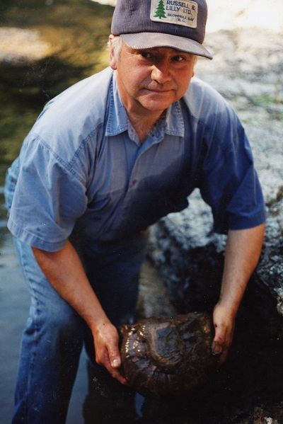Graham Beard, debout dans Englishman River, avec un regard pensif, tenant une ammonite qu’il vient juste de libérer dans ses mains. c. 2005