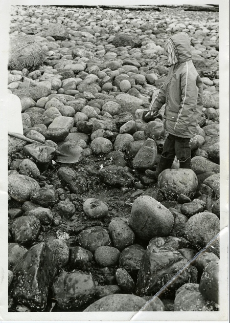 Une fille dans un coupe-vent sur une plage couverte de rochers, indiquant un endroit devant elle où les roches ont été dégagées