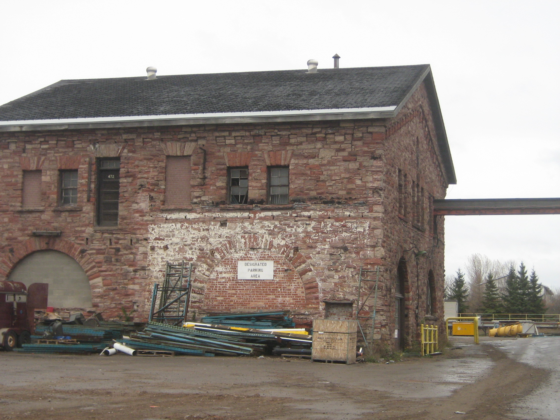 L'édifice en grès photographié un jour de grisaille avec un amoncellement de tuyaux d'acier en face du bâtiment.