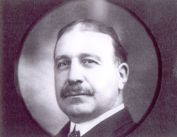 Portrait de Clergue dans un cadre circulaire. Chevelure foncée séparée au milieu, moustache bourrue. Habit noir et collet blanc.