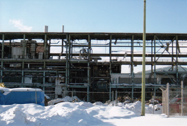 Les poutres de l'un des édifices modernes sont mises à nu durant la démolition. On aperçoit la neige en avant plan. Le bâtiment a des allures décrépites.