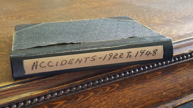 Vieux carnet noir sur une table en bois. Sur une étiquette au dos du livre est inscrit : Accidents – 1922-1948