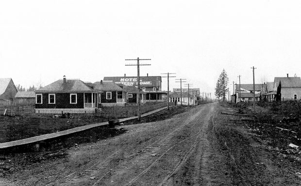 Photographie en noir et blanc du centre d’Aldergrove autour de 1900. Une route de terre traverse le village, entre les bâtiments situés de part et d’autre de celle-ci.