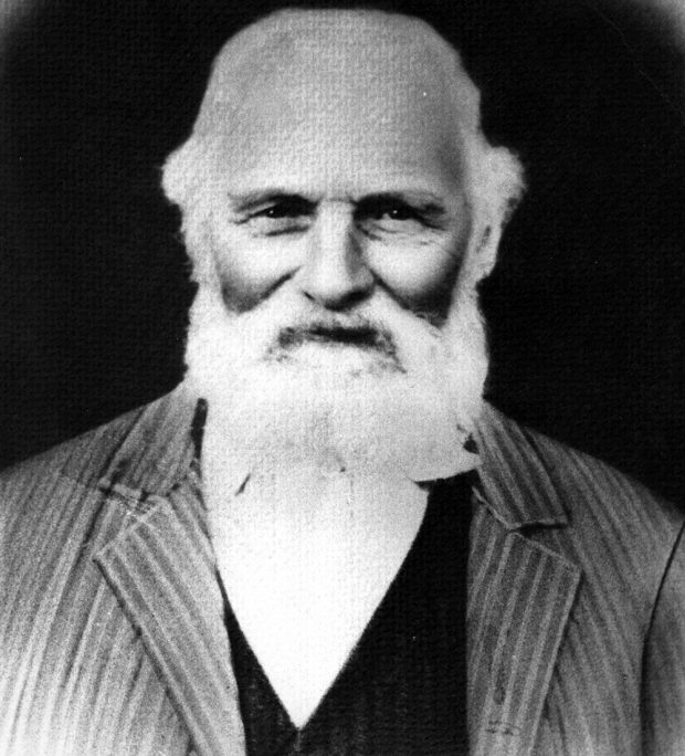 Un portrait en noir et blanc (réalisé en studio) de Philip Jackman, âgé, les cheveux et la barbe blanche. Il porte un complet à rayures, une veste foncée et une chemise pâle.