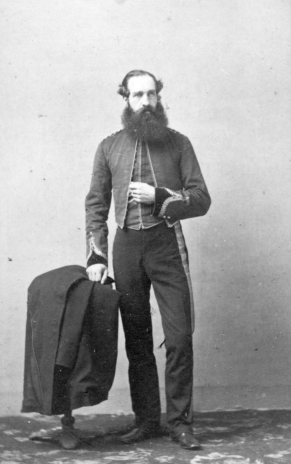 Un portrait en noir et blanc (réalisé en studio) du capitaine Henry Reynolds Luard avec sa longue barbe. Celui-ci porte un uniforme militaire; son bras gauche est replié devant son torse, et sa main droite est placée sur son manteau, qui est drapé sur une petite table.
