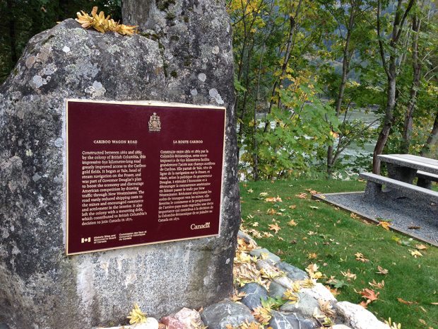 Une photo d’une plaque commémorative sur fond bourgogne fixée sur un gros bloc de granit à Yale, en Colombie-Britannique. La plaque présente les grandes lignes de l’histoire de la construction de la route d’accès à la région de Cariboo.