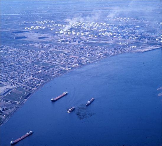 Des bateaux circulant sur un cours d'eau près d'une ville avec des raffineries de pétrole en arrière plan