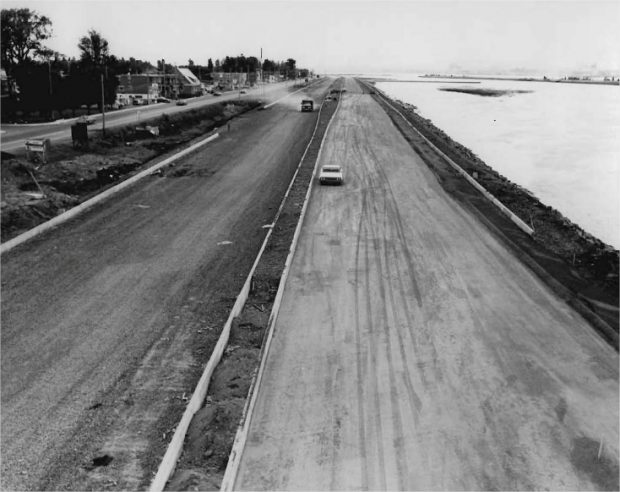 Une autoroute en construction avec des véhicules en circulation et des maisons en arrière plan