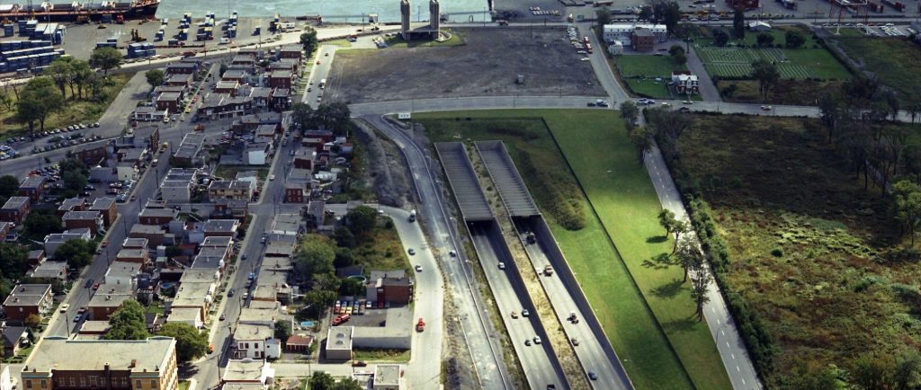 Des voitures circulant sur une autoroute avec des installations portuaires et un cours d'eau en arrière plan