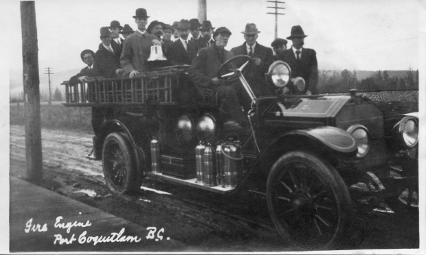 Un grand groupe d’hommes en habit chic se tient dans un camion de pompiers face à la caméra.