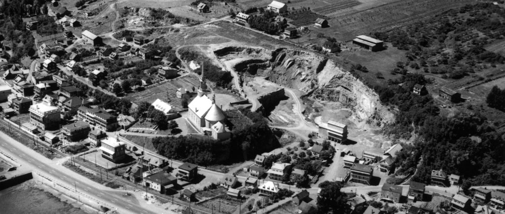 Photographie d’archives en noir et blanc. La municipalité de Château-Richer se déploie autour de l’église, qui se trouve au centre de l’image. Outre des maisons, on aperçoit une carrière de pierre, des champs cultivés, un chemin de fer et le boulevard Sainte-Anne.