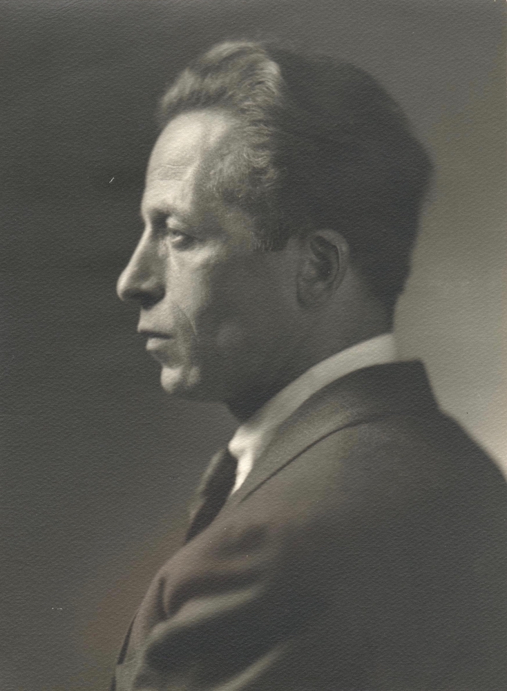 Photographie d’archives en noir et blanc montrant Albert Gilles de profil regardant vers la gauche. Il est vêtu d’un complet-cravate.