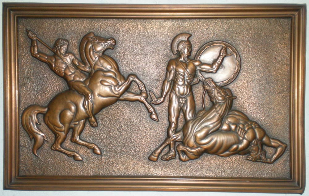 Photographie couleur d’une œuvre en cuivre repoussé montrant un guerrier à cheval armé d’une lance se préparant à attaquer un homme équipé d’un casque, d’un bouclier et d’une épée. Un troisième personnage est allongé sur un cheval blessé.