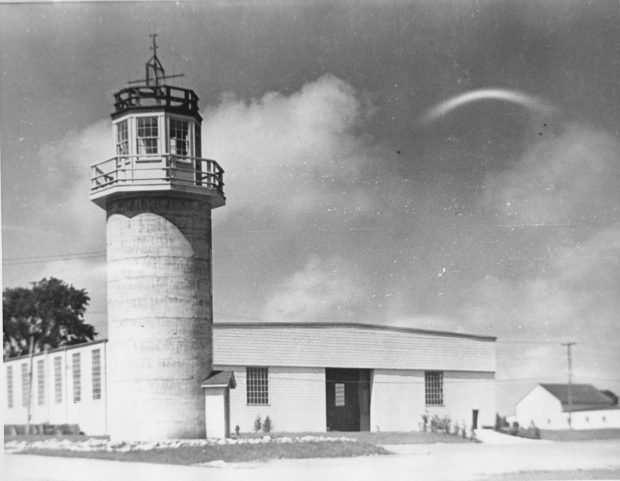 Image en noir et blanc d’une tour de guet / silo à côté d’un bâtiment bas.
