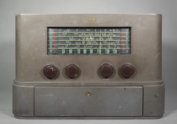 La radio de table possède un extérieur peint en gris avec des bords incurvés et aucune autre décoration. En bas se trouve un tiroir verrouillable.