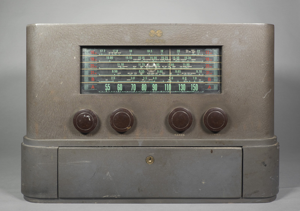 La radio de table possède un extérieur peint en gris avec des bords incurvés et aucune autre décoration. En bas se trouve un tiroir verrouillable.