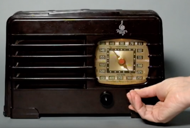 Radio Emerson de 1940 avec une main tournant un cadran sous une fenêtre d'affichage de fréquence de couleur laiton.