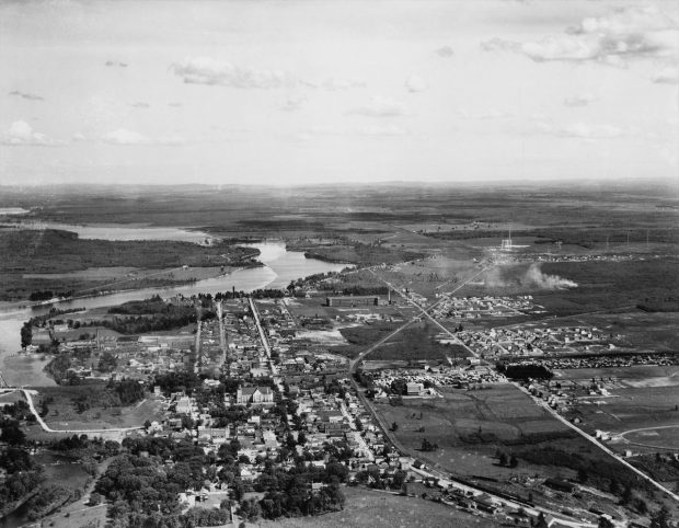 Photographie en noir et blanc démontrant une vue aérienne du centre-ville de Drummondville. On y voit les maisons, les églises, les usines, les routes ainsi que les chemins de fer.