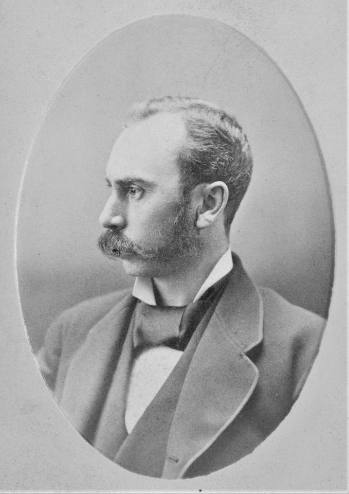 Photographie en noir et blanc d’un homme posant de profil, vêtu d’un veston et d’un foulard.