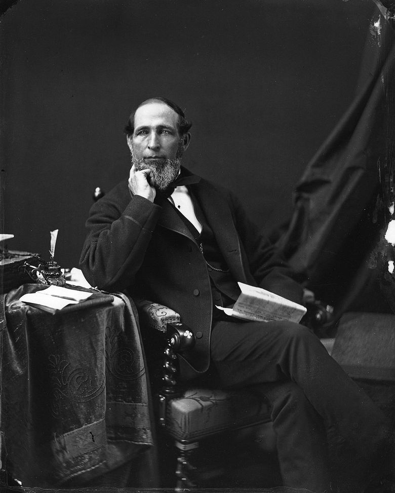 Photographie en noir et blanc d’un homme assis sur un fauteuil avec un journal à la main.