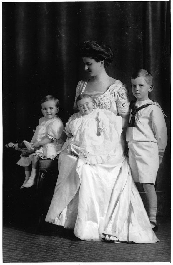 Photographie en noir et blanc d’une femme posant assise avec ses trois enfants en bas âge, le bébé sur ses genoux.