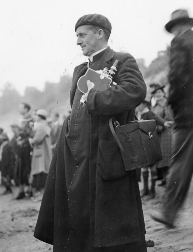 Albert Tessier se tient, caméra à la main, sur une plage au milieu d'autres spectateurs de la course de canots.