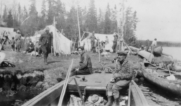 Plusieurs hommes, femmes et enfants s'affairent dans un campement rudimentaire installé sur les berges d'une rivière.
