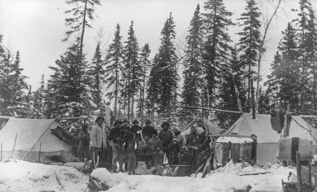 Dans la forêt, des Autochtones de tous âges posent dans la neige au milieu de tentes rudimentaires.