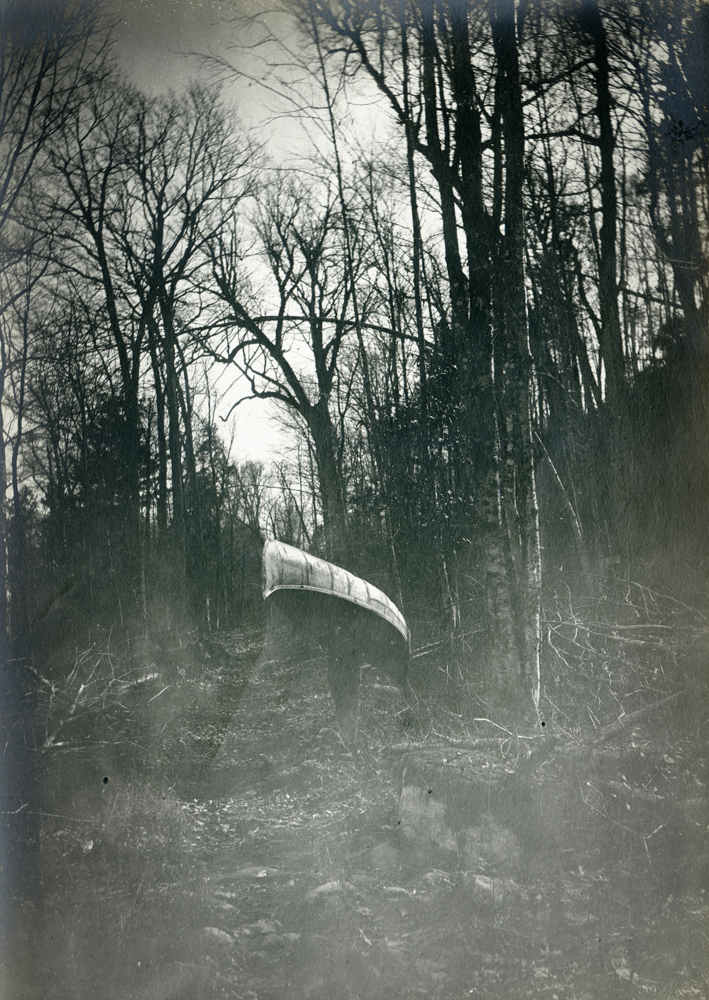 Un homme porte un canot sur ses épaules au milieu de la forêt. 