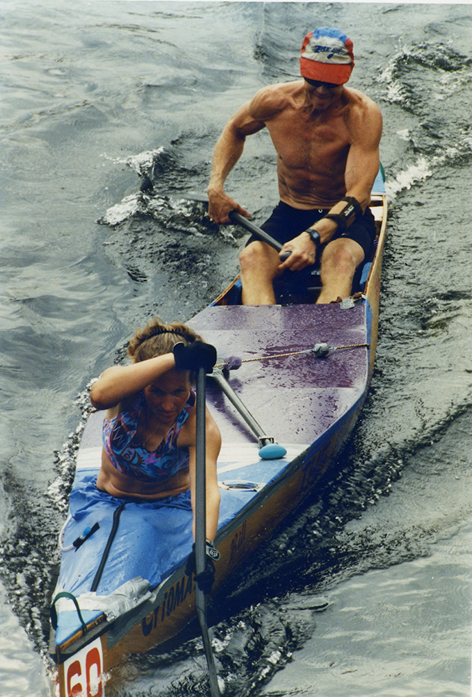 Dans un canot sont installés un homme et une femme qui rament tous deux avec force.