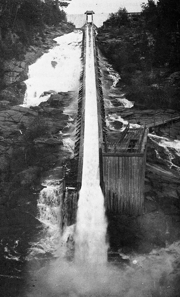 Au milieu des rochers, une grande structure de bois offre une pente droite et continue où s’écoulent l’eau et les billots de bois.