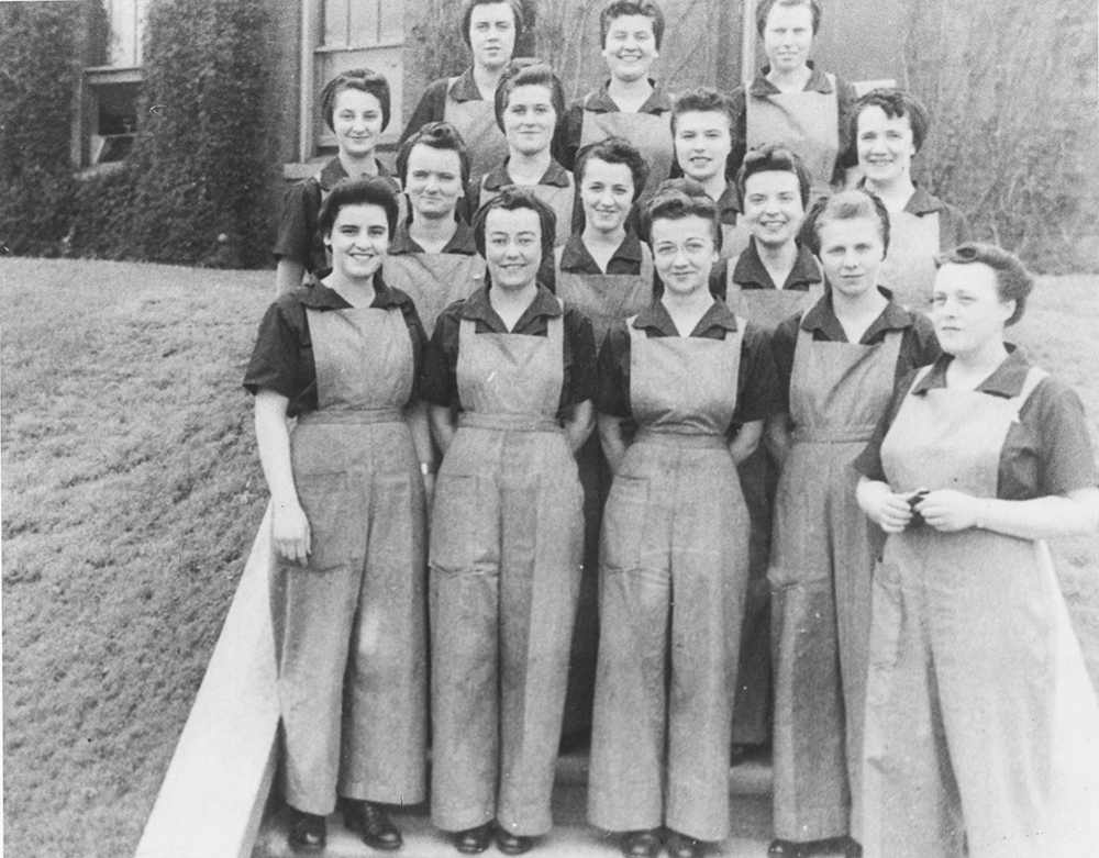 Un groupe de femmes en habit de travail pose devant un immeuble en brique 