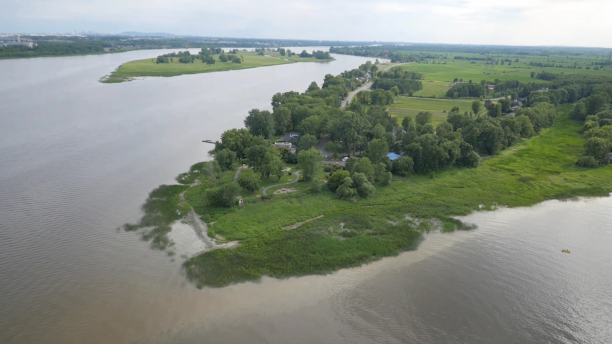 Image en couleur d’une vue aérienne de la pointe est de l’île en été. On voit la rivière des Prairies à gauche et la rivière des Mille-Îles à droite. Elles se rejoignent au bas de l’image. 