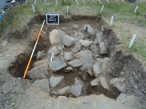 Grille assortie de mesures et échelle couchée près d’un tas de gravats de pierre située dans une excavation rectangulaire.