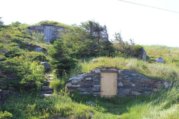 Extérieur de deux caves à légumes en pierres empilées construites à flanc de colline, avec de petites portes en bois.