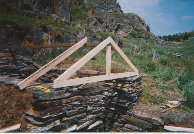  Pierres empilées à flanc de colline, sans porte, avec la structure de la remise au-dessus en cours de construction.