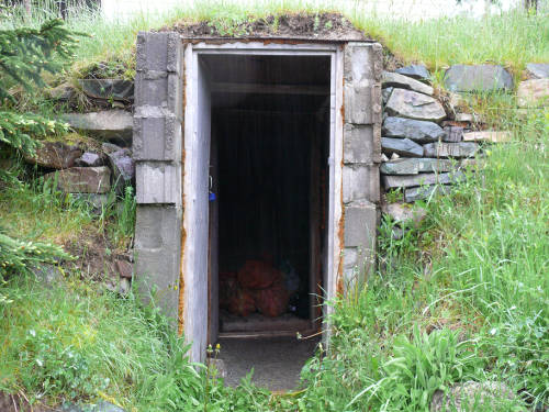 Porte rectangulaire en béton avec des pierres empilées à flanc de colline d'une cave à légumes.