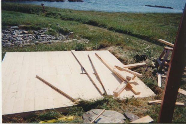 Vue de dessus du plancher de la remise d’une cave à légumes en construction, au milieu d’un champ herbeux au bord de l’océan.