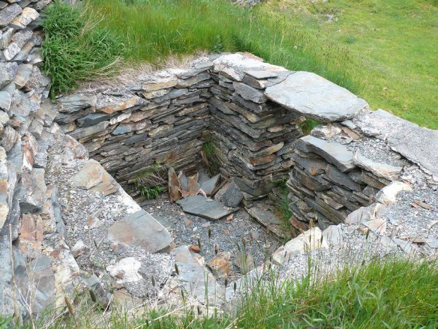 Fondation d’un mur de pierres plates empilées construit dans le flanc d’une colline couverte d’herbe.