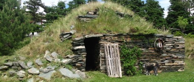 Extérieur d’une cave à légumes à flanc de colline, avec façade en pierres empilées et dessus recouvert d’herbe.