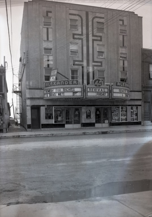 Photographie en noir et blanc d’un bâtiment à quatre étages avec un cinéma au rez-de-chaussée. Les noms des films à l’affiche sont inscrits sur la façade.