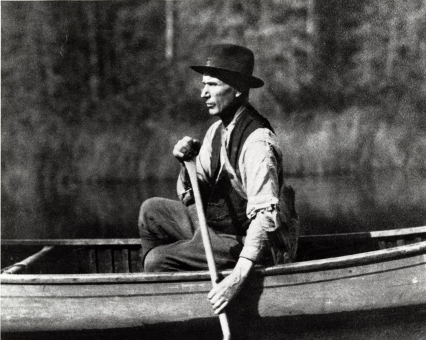 Photo en noir et blanc du prospecteur qui pagaye sur un lac avec la forêt en arrière-plan.